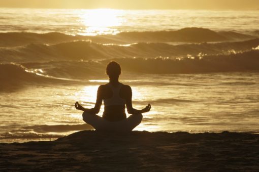 Woman meditating on beach at sunrise